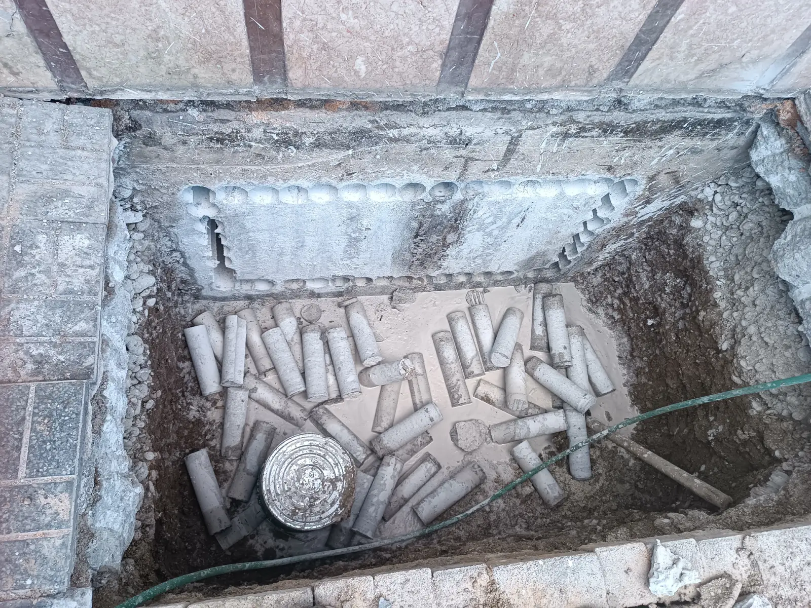 Toprak seviyesinin altındaki beton perdede sıralı karot delikleriyle çevrelenmiş dikdörtgen açıklık; çukurda delmeden çıkan beton karot çekirdekleri